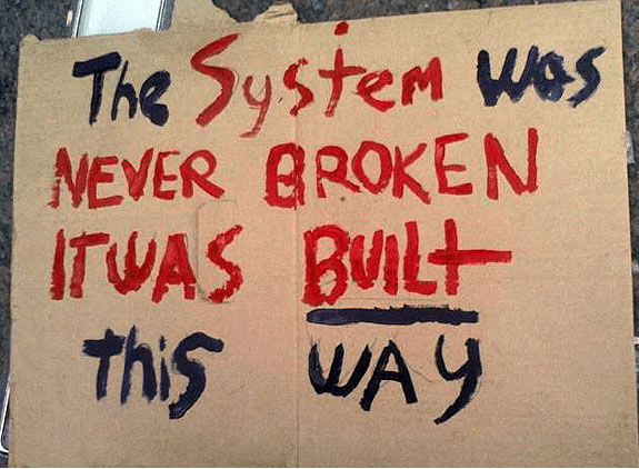 A sign that says the system was never broken it was built this way - Kathbern Management - Toronto Recruiting Agency